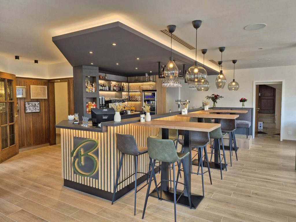 Moderne Theke mit Holzverkleidung aus vertikalen hellen Holzleisten mit dunklen Vertiefungen in Leistenbreite, ideal für Ihre Gastronomie. Der Thekenrückschrank ist in der gleichen Optik. Das Thekenbrett ist in einem dunkelgrau bis schwarz